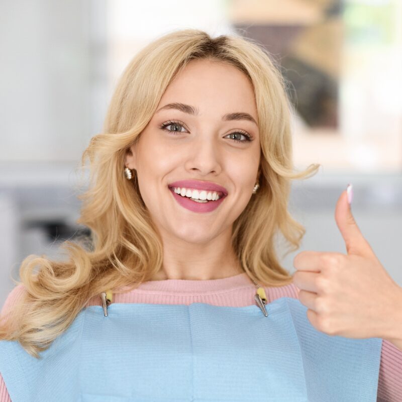 young woman smiling in a dental chair giving a thumbs up