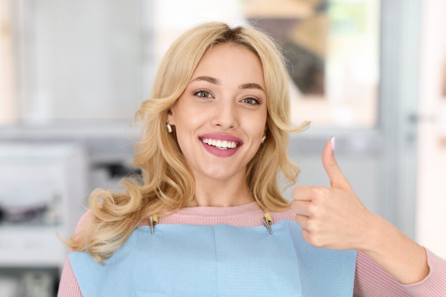 young woman smiling in a dental chair giving a thumbs up